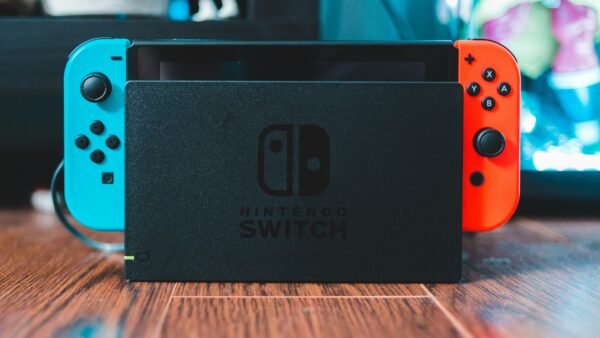 Nintendo Switch colocada en su base de carga con mandos Joy-Con azul y rojo sobre una superficie de madera