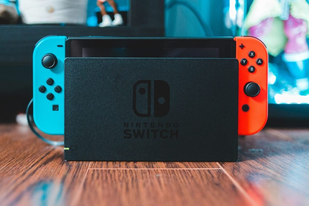 Nintendo Switch colocada en su base de carga con mandos Joy-Con azul y rojo sobre una superficie de madera