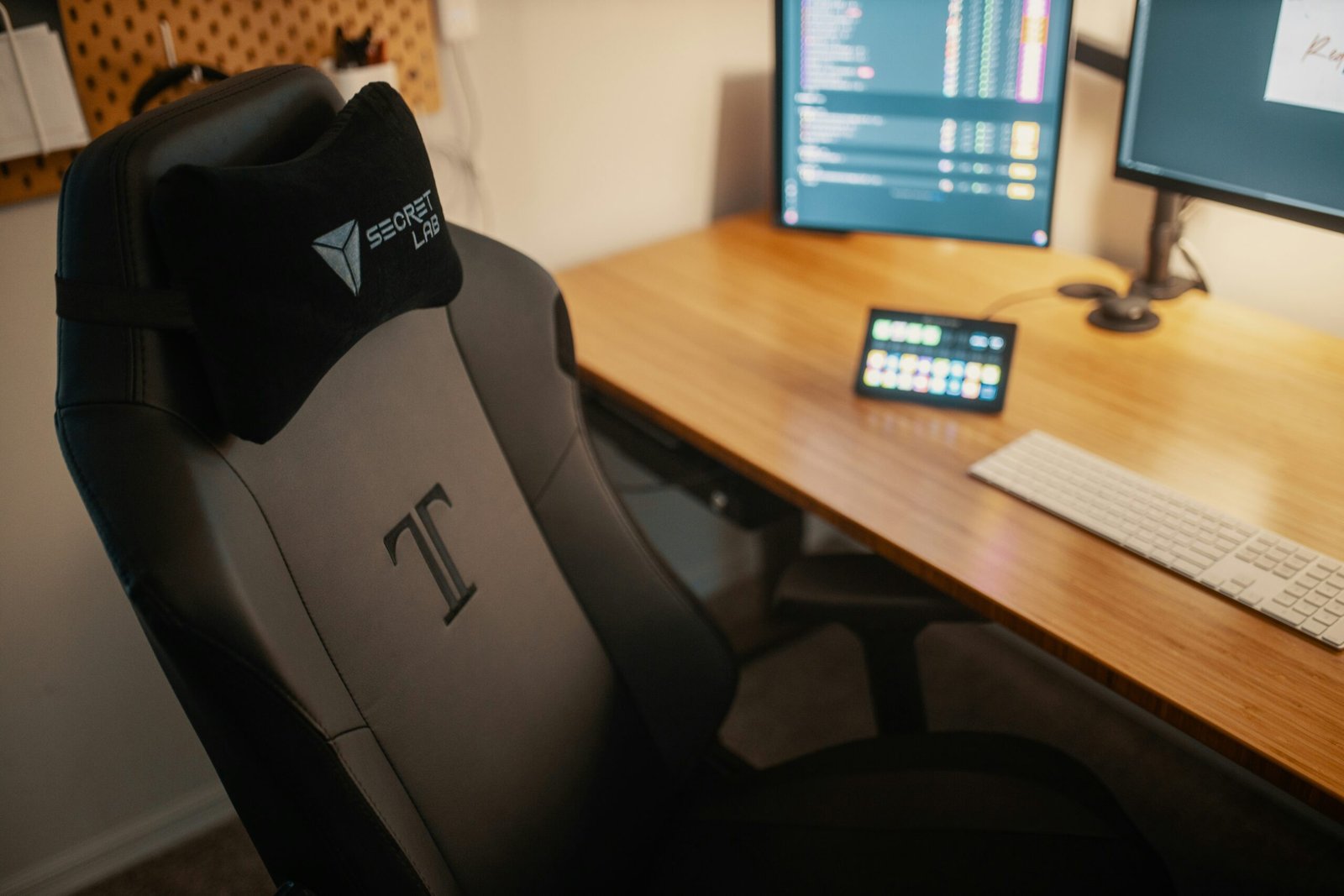 Silla gaming negra junto a un escritorio de madera con doble monitor y setup de trabajo moderno.
