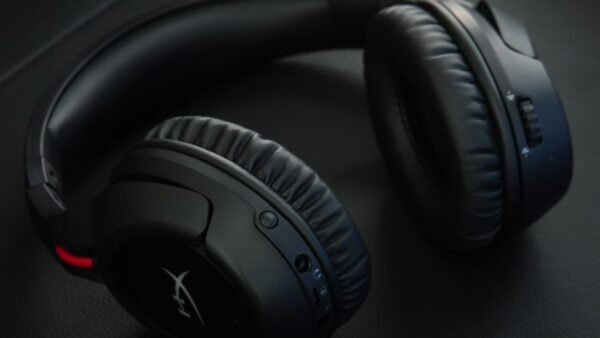 Auriculares gaming inalámbricos negros sobre una superficie oscura, con diseño circumaural y controles integrados para audio y comunicación.