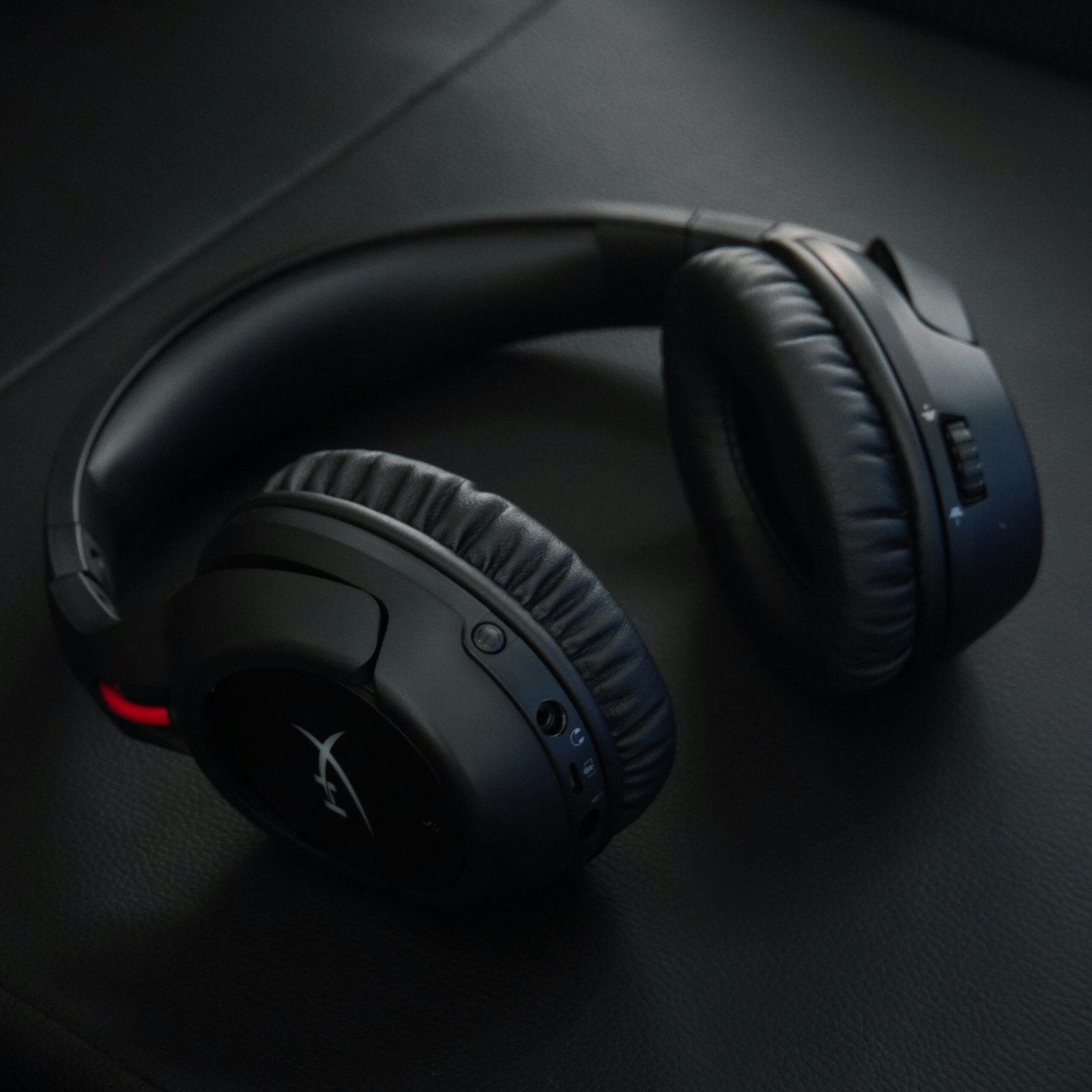 Auriculares gaming inalámbricos negros sobre una superficie oscura, con diseño circumaural y controles integrados para audio y comunicación.